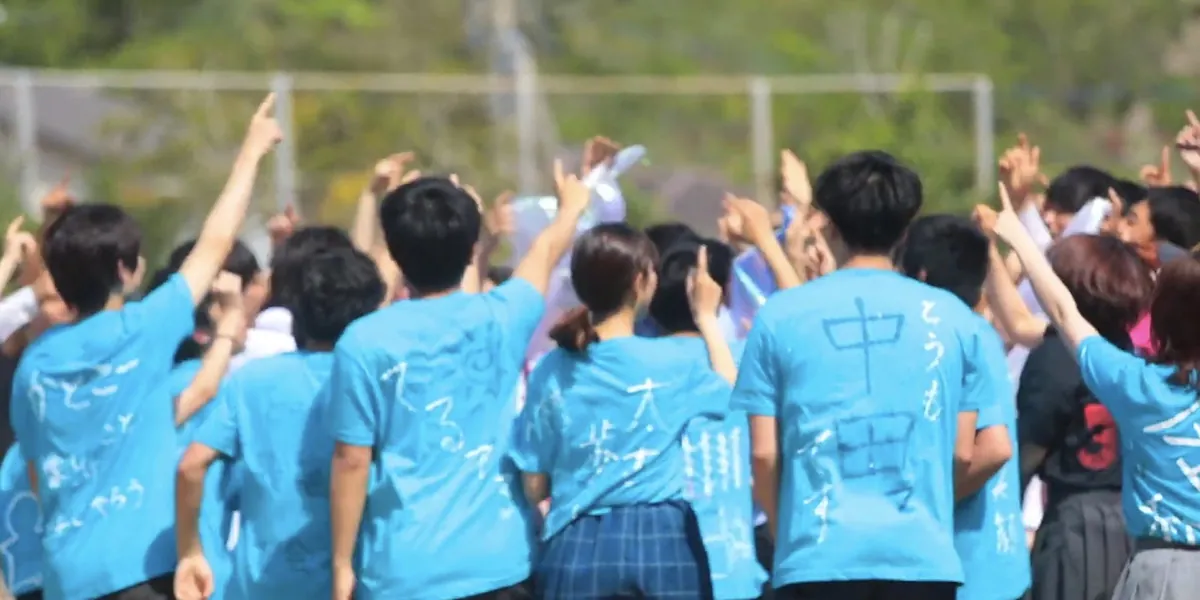 そろいの水色のTシャツで手を挙げる後ろ姿