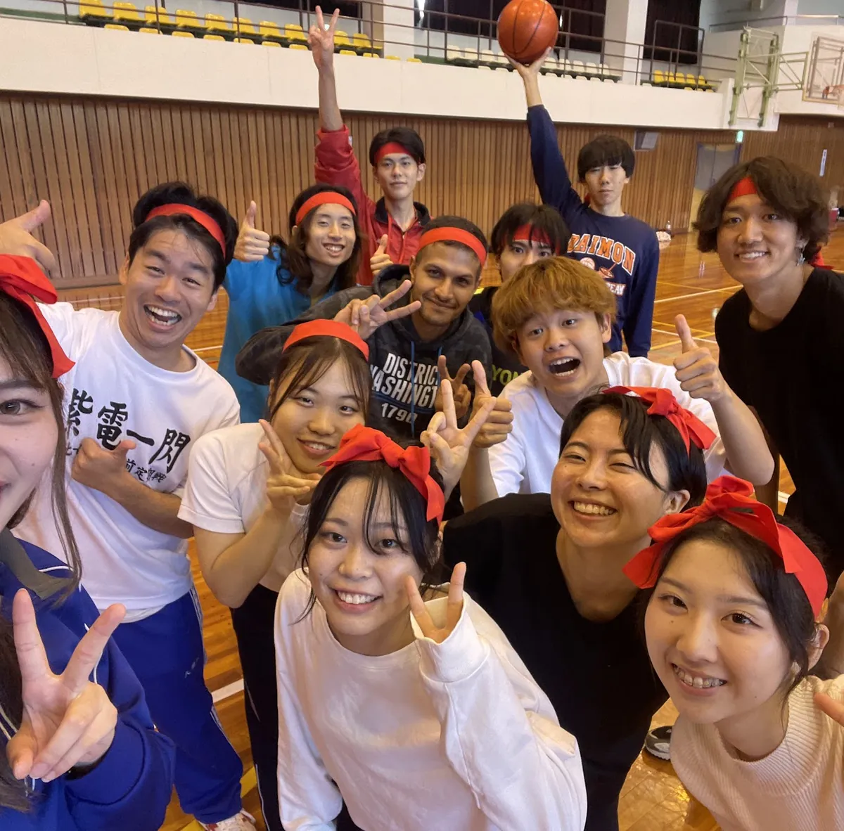 赤い鉢巻をして、体育館で笑う人たち
